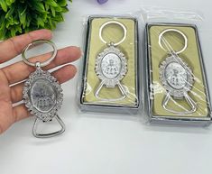 two silver key chains are sitting next to each other on a white table with flowers in the background