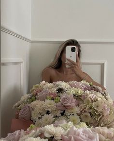 a woman taking a selfie in front of a bouquet of flowers with her phone