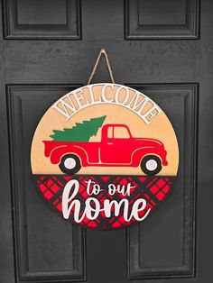 a red truck with a christmas tree on it is hanging from the front door and welcome to our home sign