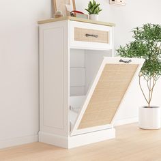 a white cabinet with a door open and a potted plant in the corner next to it