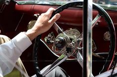 an old man driving a classic car with his hands on the steering wheel