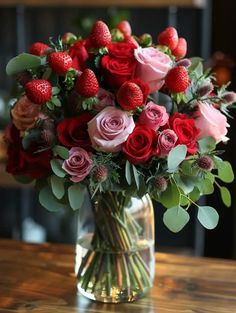 a vase filled with lots of red and pink flowers on top of a wooden table