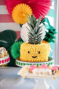 a pineapple cake with sprinkles is on a table next to cupcakes