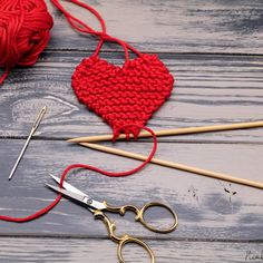 two crocheted hearts are next to knitting needles and yarn