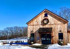 a barn with a wreath on the door and snow covered ground in front of it