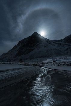 the moon shines brightly in the sky over a snowy mountain range, with a stream running through it