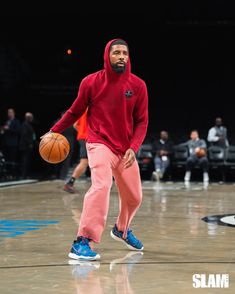 a man in a red hoodie holding a basketball on a court with people watching