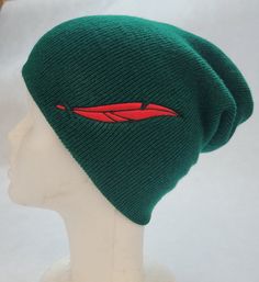 a green beanie hat with a red feather on the front and side, sitting on top of a mannequin head