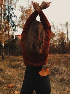 a woman standing in a field holding her hands up above her head and looking at the sky