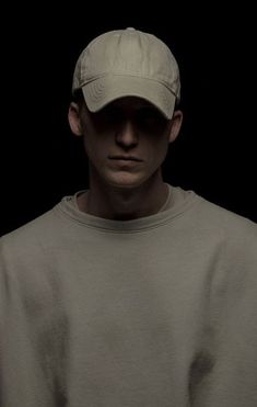 a man wearing a baseball cap in front of a black background with his head turned to the side