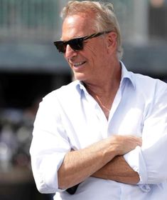 an older man with his arms crossed wearing sunglasses and a white shirt is smiling at the camera