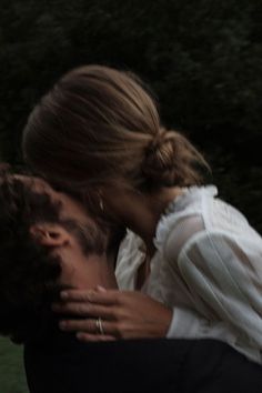 a man and woman kissing each other in front of trees