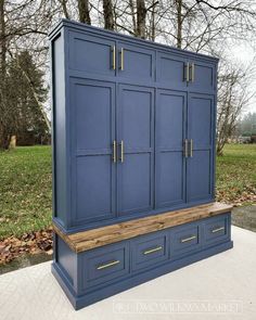 a blue armoire sitting on top of a wooden bench in front of some trees