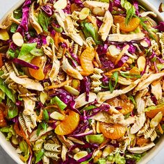 a salad with oranges, chicken and pasta in a white bowl on a table