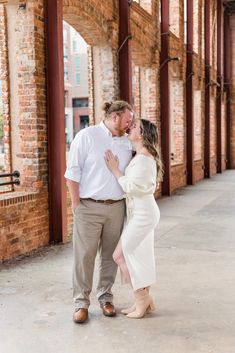 a man and woman standing next to each other in front of brick building with arches