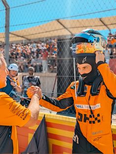 a man in an orange jacket is shaking hands with another man wearing a black helmet