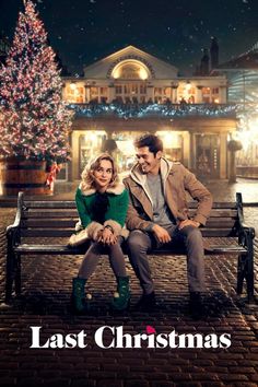 a man and woman sitting on top of a bench in front of a christmas tree