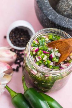 a jar filled with pickled vegetables next to garlic and pepper on a pink surface