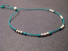 a blue string bracelet with white beads and silver beads on the end, sitting on a gray surface