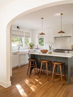 a kitchen with two stools in front of an island and white cabinets on the wall