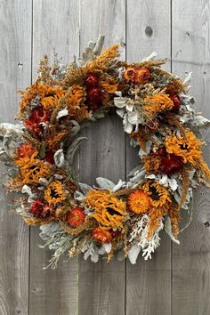 a wreath with orange and red flowers hanging on a wooden wall next to a fence