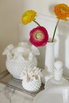 three colorful flowers are in white vases on a bathroom countertop next to a sink