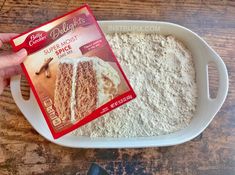 a person holding a package of cake mix in front of a white plate on a wooden table