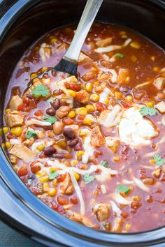 a crock pot filled with chicken, beans and tortilla soup next to a wooden spoon