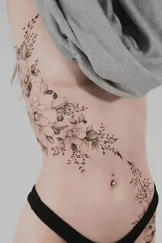 a woman's stomach with flowers and leaves on her side, showing the tattoo