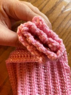 a hand holding a pink knitted object on top of a wooden table