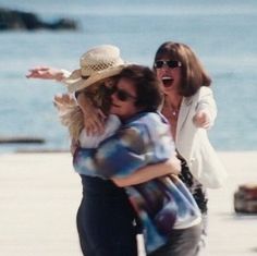 two women are hugging each other on the beach while another woman is holding her arms around them