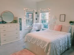 a white bed sitting in a bedroom next to a window with lights on it's sides