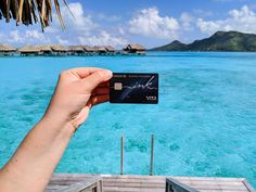 a person holding up a credit card in front of the ocean with over blue water