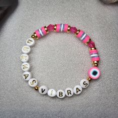 "The Buenas Vibras Good Vibes Beaded Word Bracelet was made using 6mm crystal bicone beads, circular spacer beads, and heishi clay beads. The words \"BUENAS VIBRAS\" are spelled out on white round letter beads in black writing. A pink polymer clay evil eye bead adorns the band of the bracelet.  Bracelets are all HANDMADE with love and care by myself, Candice Marie, and they are always limited edition and one-of-a-kind. ❤️ The bracelet is stretchy and stackable and looks great stacked with other Pink Bracelets With Spacer Beads For Festival, Festival Bracelets With Letter And Round Beads, Festival Bracelet With Letter Beads, Pink Beaded Bracelets For Festival, Spiritual Letter Beads Bracelets For Beach, Spiritual Beach Bracelets With Letter Beads, Pink Letter Beads Stretch Bracelet For Festival, Festival Stretch Bracelet With Letter And Round Beads, Pink Festival Stretch Bracelet With Letter Beads