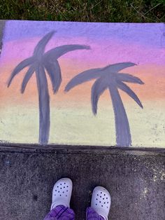 someone's feet are standing in front of a sidewalk with palm trees painted on it