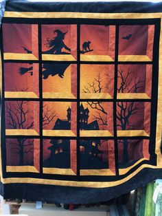 a quilt hanging on the wall in front of a window with silhouettes of witches and cats