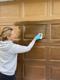 a woman in blue gloves is painting a garage door with brown wood paneling and white paint