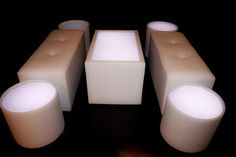 four white lit up stools sitting next to each other on a wooden floor in front of a black background