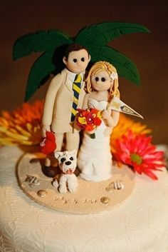 a wedding cake topper with a bride and groom on the beach holding a dog