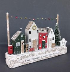 a christmas village is displayed on a wooden plank with lights and garlands around it