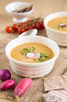 two white bowls filled with soup next to some vegetables and crackers on a table