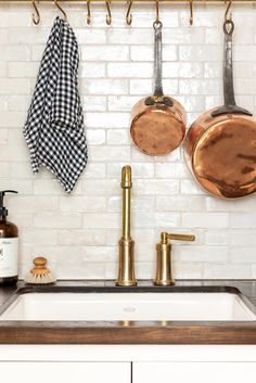 copper pots and pans hang on the wall above a kitchen sink