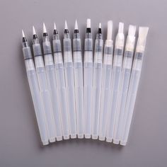 six white and black ink pens lined up in a row on a gray surface with one pen pointed at the top