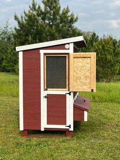 a small red and white chicken coop in the grass