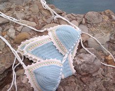 a crocheted blue and white bikinisuit laying on rocks next to the water