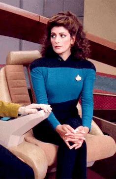 two women in star trek outfits sitting next to each other with their hands on the chair