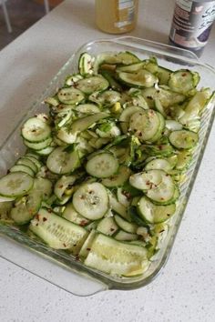 a glass dish filled with sliced cucumbers on top of a white countertop