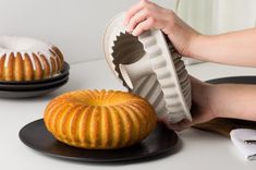 two bundt cakes sitting on top of plates next to each other, one being held by a woman's hand