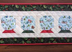 a quilted table runner with three snow globes on the top and holly trees in the bottom