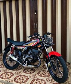 a red and black motorcycle parked on top of a tiled floor next to a wall